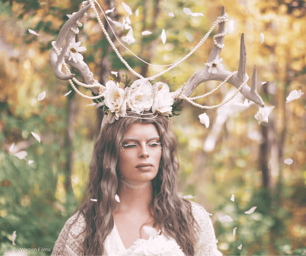 A woman wearing a deer antler crown in the woods.