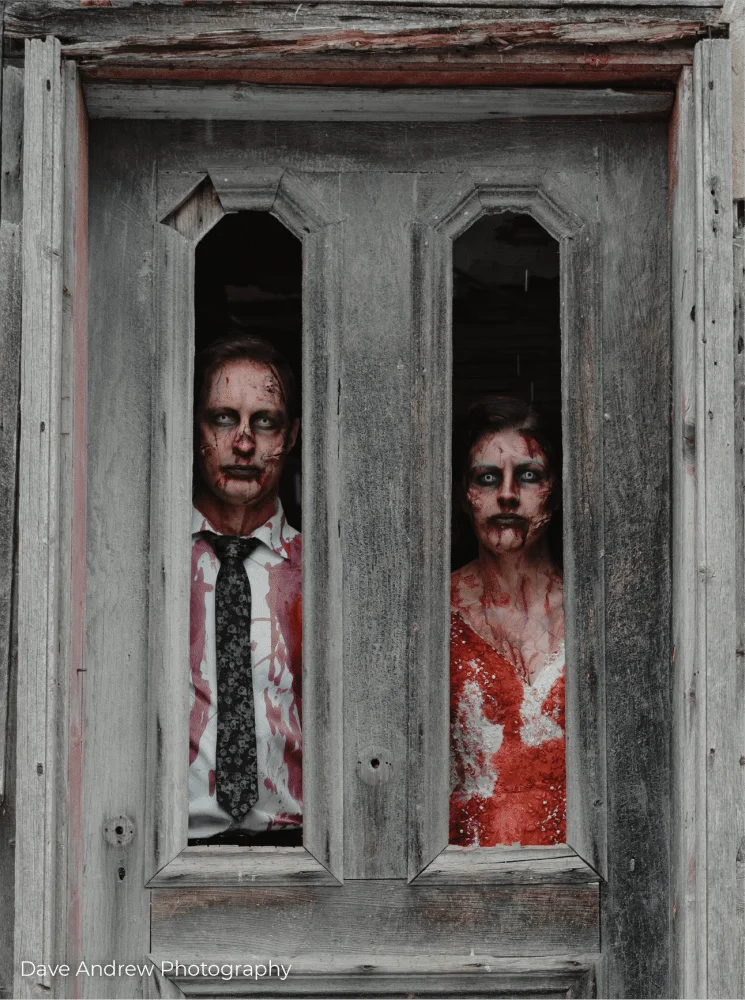 A man and woman dressed in zombie makeup are standing in a doorway.